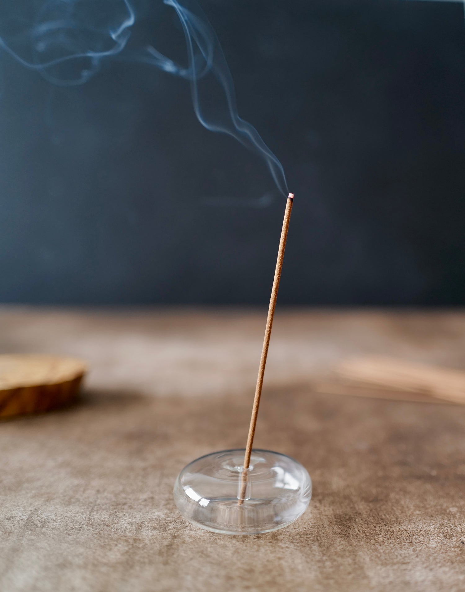 Burning Palo Santo wood incense stick releasing smoke in a clear glass holder.